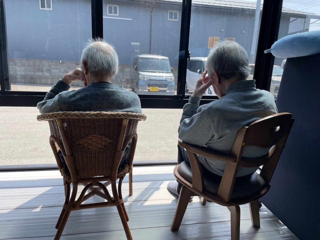 大きな窓から外の景色を眺める2人の入居者が座っている共用スペース